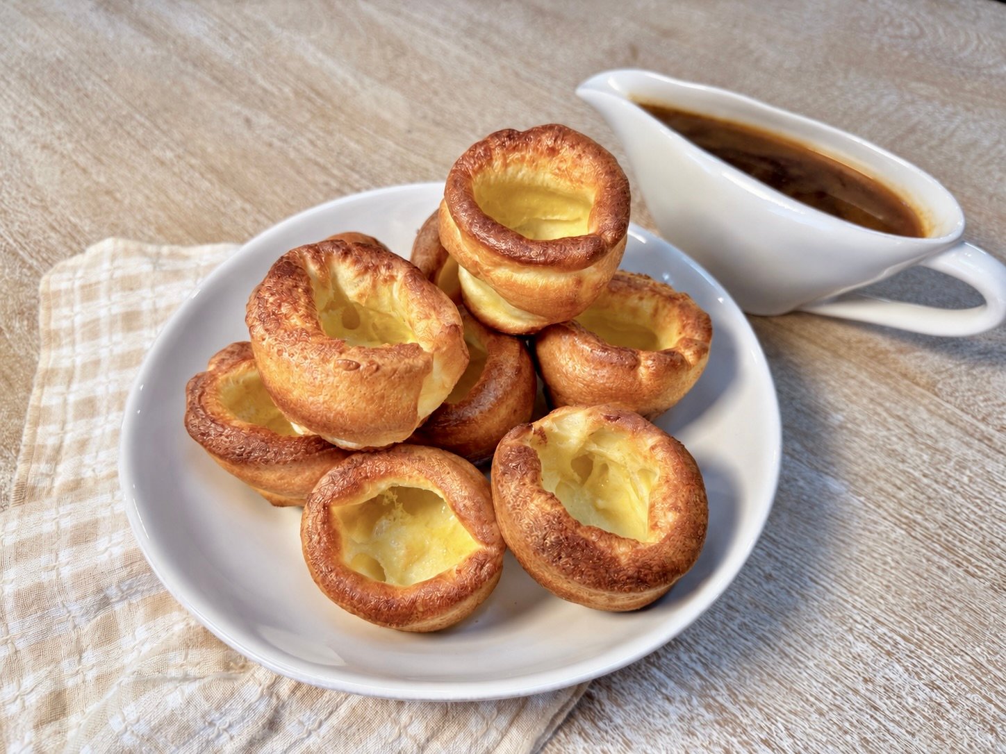 Golden Yorkshire puddings with crisp edges arranged on a white plate with a boat of gravy