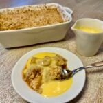 Apple crumble served warm with custard, with the baking dish and custard jug in the background