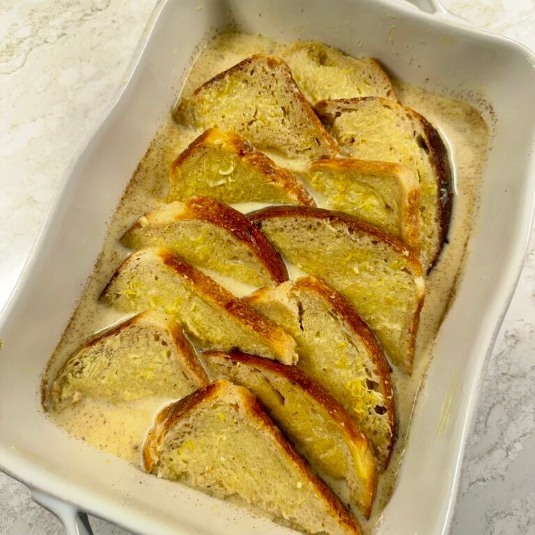 Buttered bread covered in vanilla custard in a baking dish, ready to be baked.