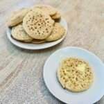 Stack of British Crumpets on a plate with an individual buttered crumpet on another smaller plate