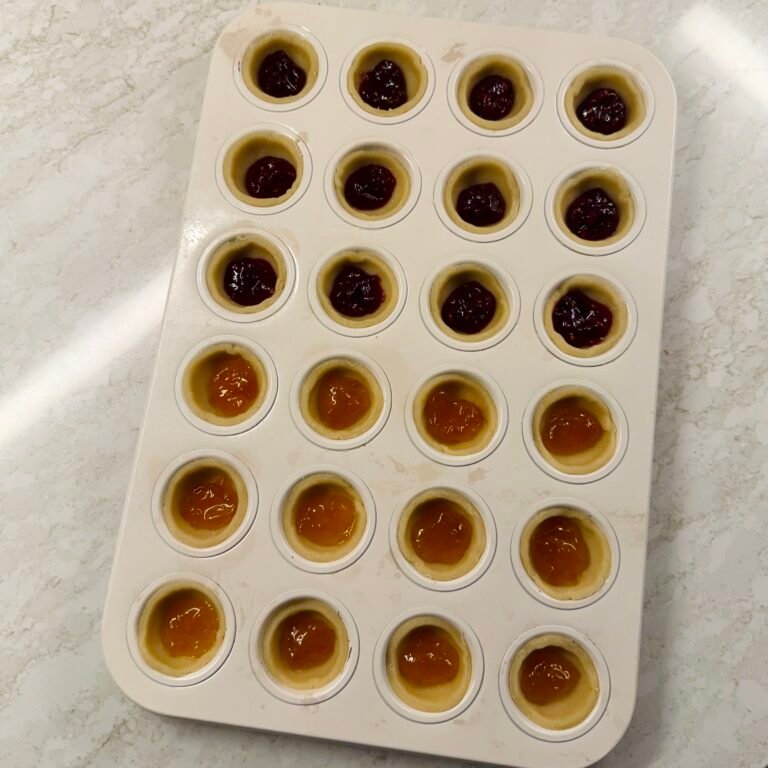 Unbaked jam tarts filled with raspberry and apricot jam in a 24-cup mini muffin tin, ready for baking.
