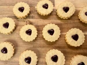 Homemade British Jammy Dodgers with fluted edges, heart-shaped centers, and raspberry jam filling.