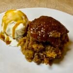 Golden sticky toffee pudding with vanilla ice cream and toffee sauce on a plate.