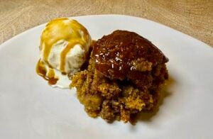 Golden sticky toffee pudding with vanilla ice cream and toffee sauce on a plate.