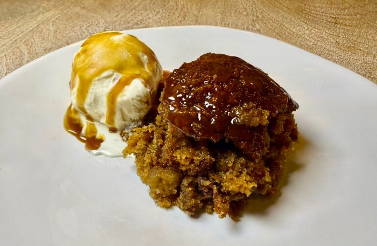Golden sticky toffee pudding with vanilla ice cream and toffee sauce on a plate.