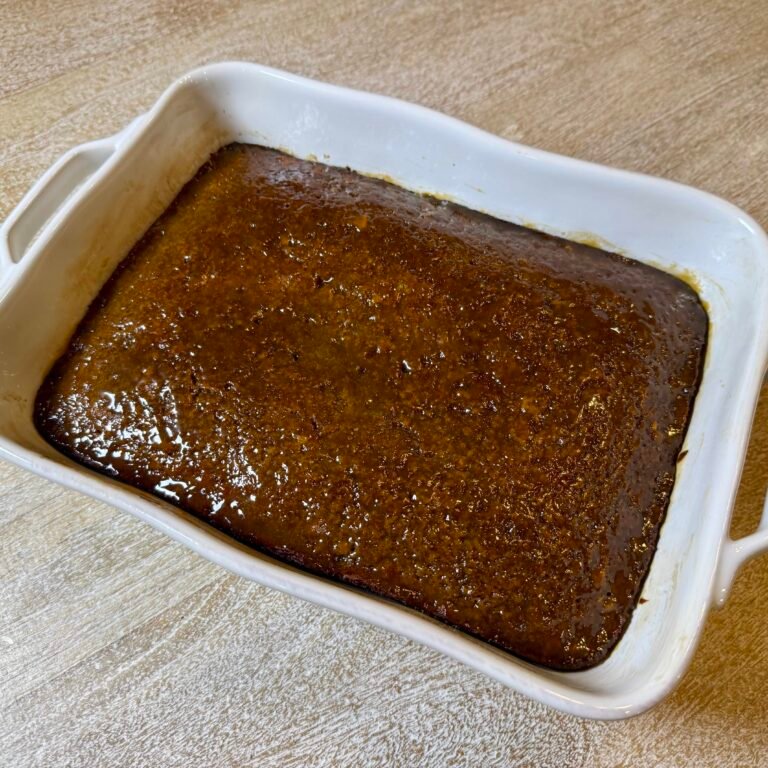 Freshly baked sticky toffee pudding in a white baking dish,.