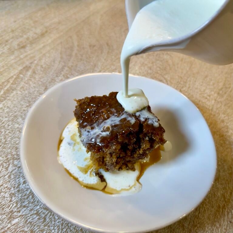 Serving of sticky toffee pudding with cream being poured over its